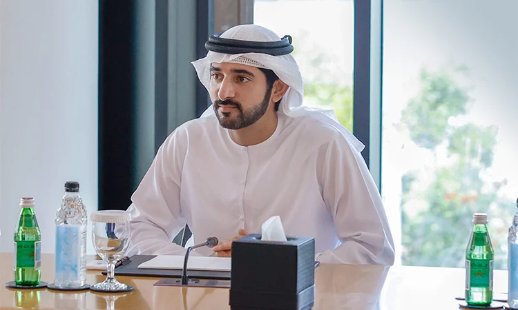 Son Altesse Sheikh Hamdan bin Mohammed bin Rashid Al Maktoum, prince héritier de Dubaï, assis à une table de réunion, vêtu de la tenue traditionnelle émiratie, prêt à participer à une discussion officielle.