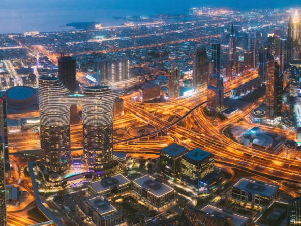 Vue aérienne nocturne de Dubaï, mettant en lumière les gratte-ciel illuminés et l’architecture moderne emblématique de la ville. Paysage urbain vibrant reflétant le dynamisme économique et le développement vertical de la métropole.